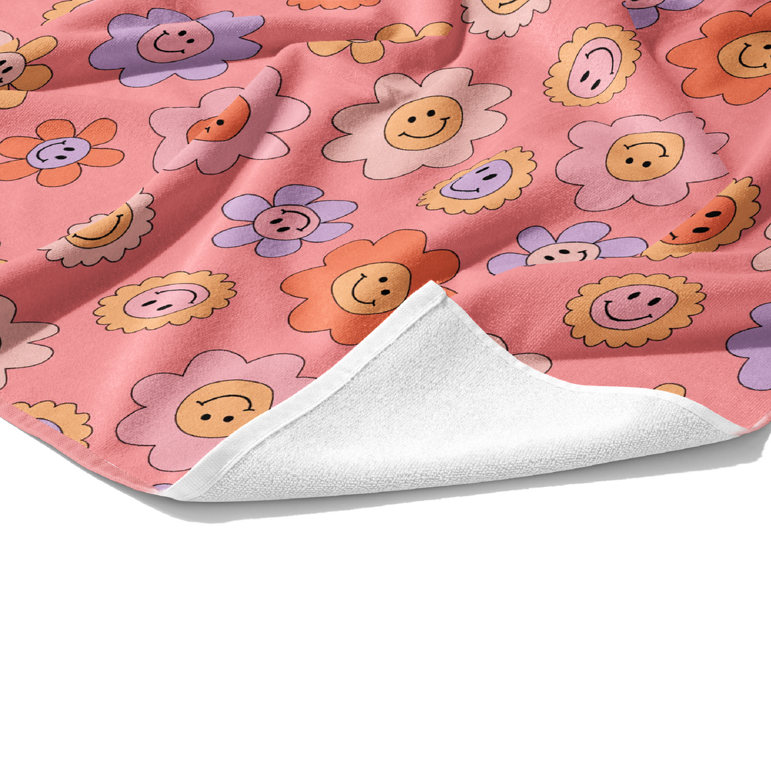 Plush white cotton personalized towel with light peach, lavender, pale yellow, and coral daisies with smiley face print on the front.
