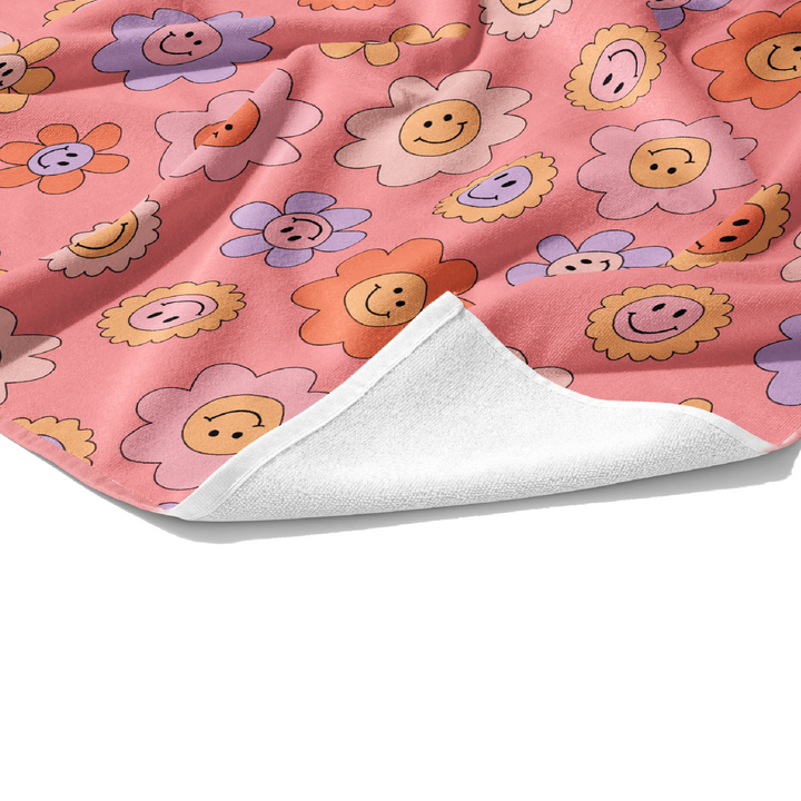 Plush white cotton personalized towel with light peach, lavender, pale yellow, and coral daisies with smiley face print on the front.