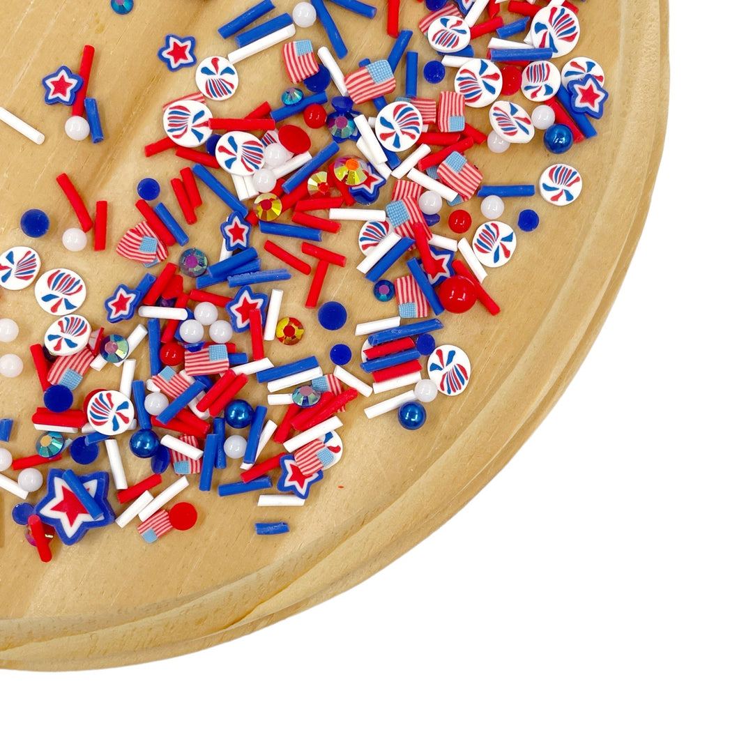 A variety of red, white, and blue polymer clay pieces arranged on a wooden surface, including stars, stripes, and round shapes.

This loose clay mix is sold in a resealable 1 oz Bag

- Material: Polymer Clay and Glitter
