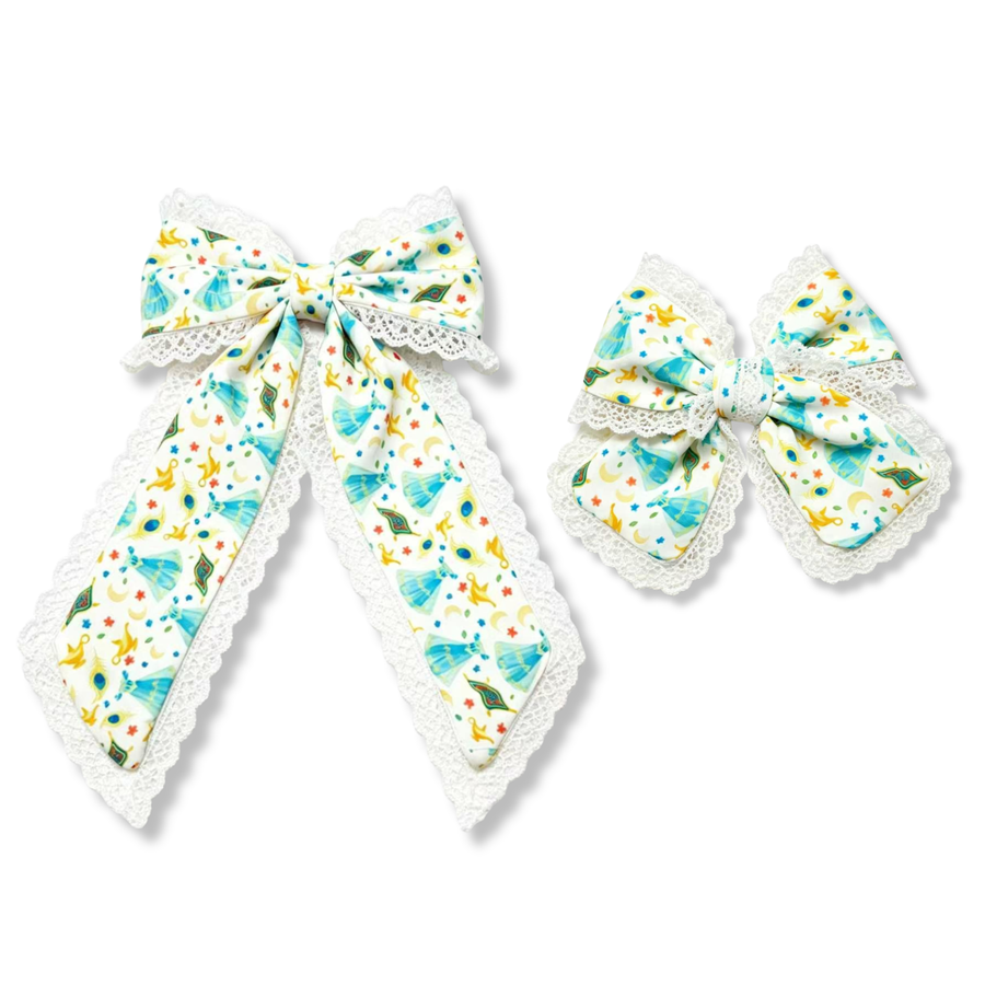 This elegant fairytale-inspired bow features a soft white ribbon printed with turquoise princess gowns, golden magic lamps, peacock feathers, crescent moons, stars, and colorful storybook accents. Delicate white lace trim frames the edges of the bow and tails, adding texture and a touch of vintage charm. The classic bow silhouette is finished with a matching center wrap and long flowing tails, creating a graceful and whimsical design.
SIZE:
Large 5.5" X 9.5"
Small 5" X 6"
