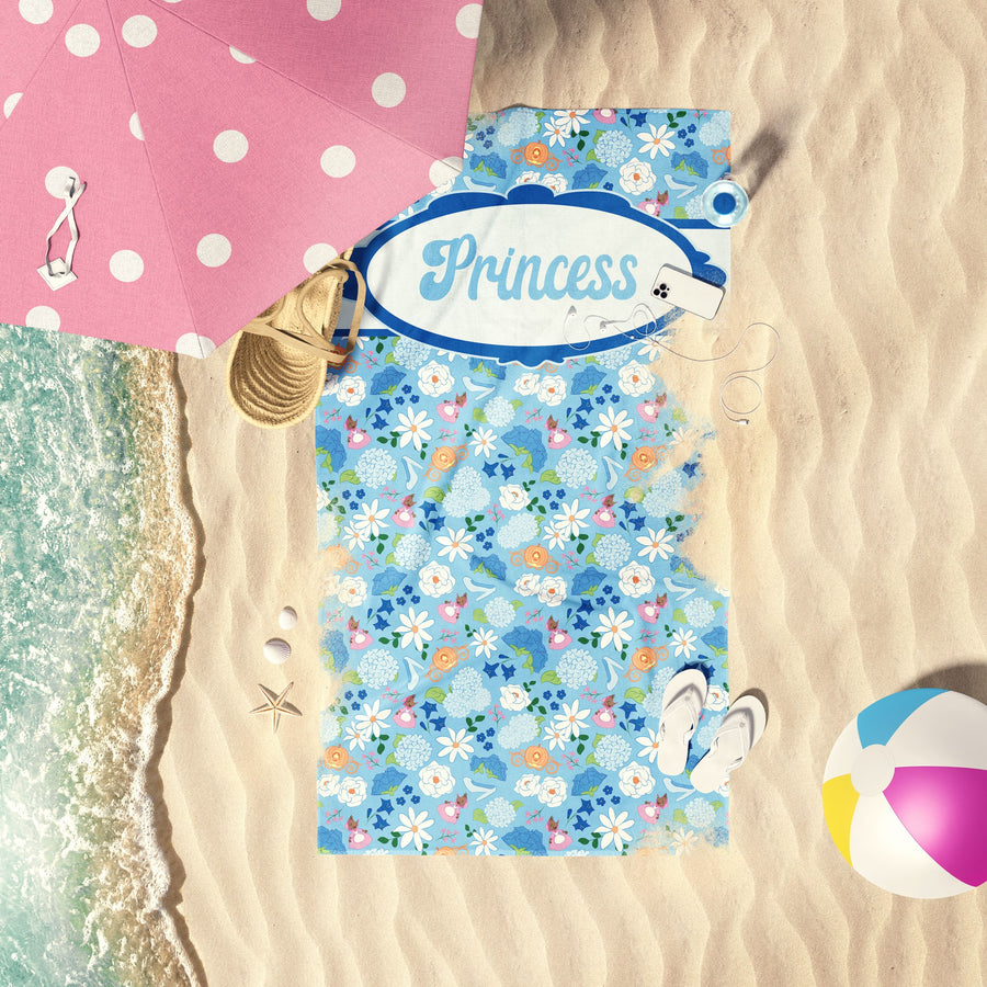 Blue Floral princess beach towel with personalized text layed out on the beach shore.