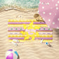 lavender and Gold princess stripe print beach towel laid out by the beach.