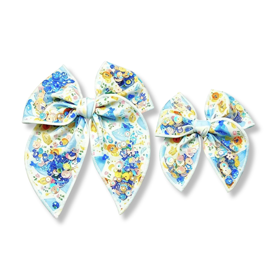 This enchanting princess-inspired bow features a white background adorned with elegant blue gowns, sparkling tiaras, glass slippers, enchanted accessories, and other fairytale-themed details. Clusters of shimmering blue, gold, and iridescent sequins are incorporated throughout the bow, adding texture, dimension, and magical sparkle across both the loops and tails. Available in both a larger and smaller size.
Small 4.5" x 4.5"
Large 6.5" x 6.5"