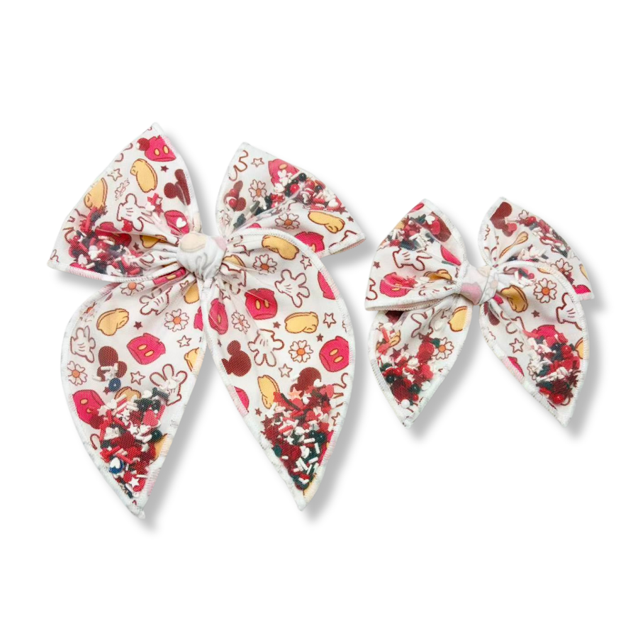 This adorable shaker bow features a white ribbon printed with classic character-inspired icons, including gloves, shoes, mouse silhouettes, flowers, and playful accents in shades of red, yellow, black,  and white. Filled with sparkling matching color sequins and confetti-like embellishments inside the shaker sections, the bow creates eye-catching dimension and movement. Available in both a larger statement size and a smaller matching style
choose size 
Small 4.5" x 4.5"
Large 6.5" x 6.5"