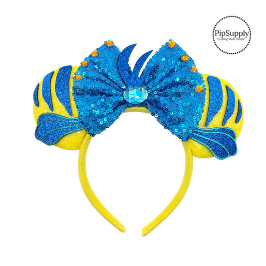 These blue and yellow mouse ear headbands are a stylish hair accessory. These comfortable headbands have attached a blue glitter bow and fish inspired glitter mouse ears. Along with a blue rhinestone embellishments. This hair accessory comes completely assembled and is great for park vacations, costumes or for everyday wear!