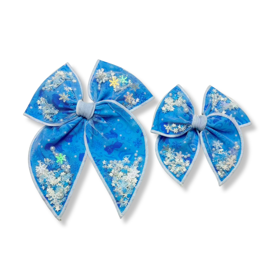 A magical winter-inspired shaker bow featuring icy blue fabric with delicate snowflake details and a sheer overlay. The shaker pockets are filled with sparkling snowflake confetti, iridescent accents, and pearl embellishments that create beautiful movement and shimmer. With its frosty color palette and enchanting sparkle, this bow captures the wonder of a snowy winter day. ❄️🩵✨🤍
Small 4.5" x 4.5"
Large 6.5" x 6.5"