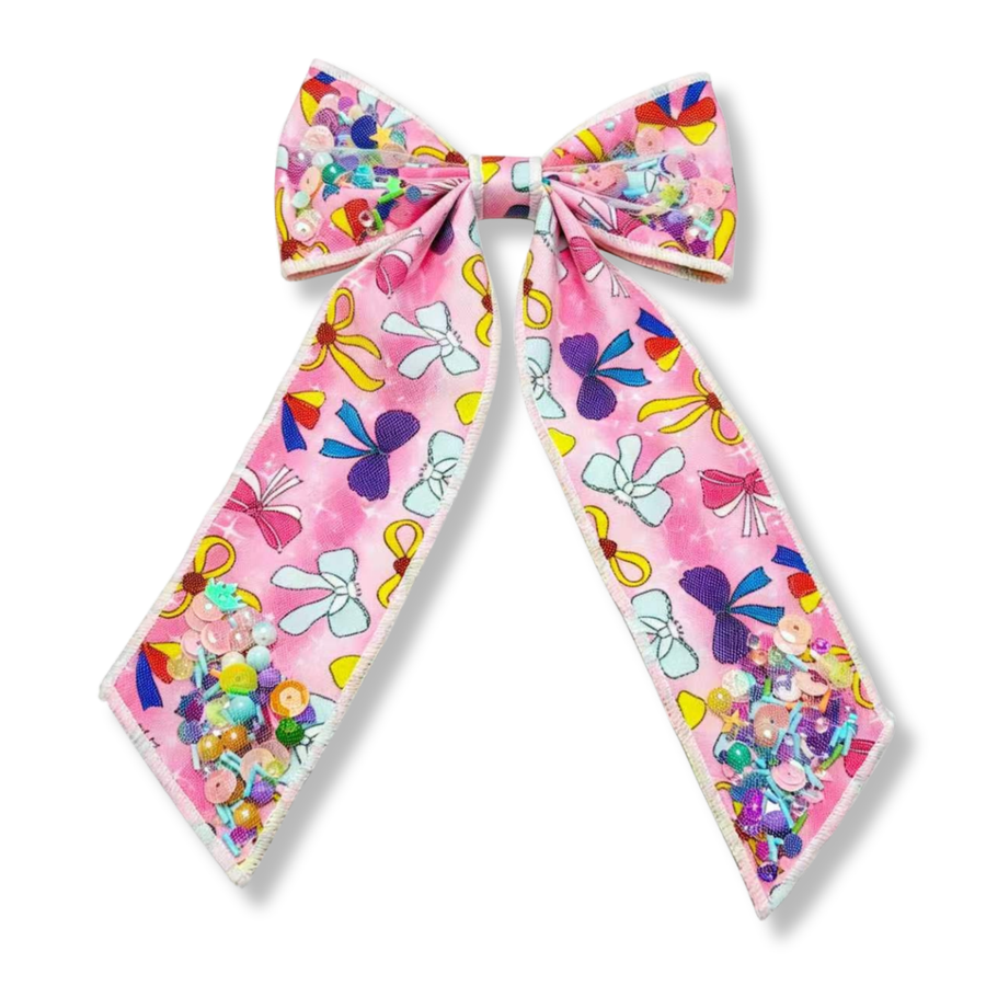 The bow features a soft pink variant background with colorful ribbon and bow prints in shades of light blue, purple, yellow, red, white, and pink. The shaker accents contain iridescent sequins, pearls, and beads in pastel and bright tones, including pink, blue, yellow, green, purple, and orange, adding a vibrant, sparkly finish.
Bow Sizing 5" x 8.5"
