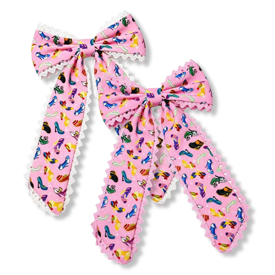 Long tail bows made from pink fabric printed with colorful shoe and accessory designs in shades of blue, yellow, green, purple, red, and black. The bows feature long flowing tails and are finished with delicate lace trim, one with white lace and one with pink lace, adding a soft, feminine touch to the playful and vibrant design.
you choose pink or white lace trim

Large 5.5" X 9.5