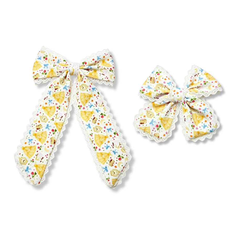 This whimsical princess-inspired bow features a crisp white background adorned with elegant yellow gowns, enchanted clocks, slices of cake, bows, flowers, stars, and other fairytale-inspired details in soft pastel colors. Delicate white lace trim accents the edges, adding a classic and elegant touch. The long tails create a graceful silhouette, while the playful storybook print brings a magical charm perfect for princess lovers and special occasions. 

choose size 
SIZE:
Large 5.5" X 9.5"
Small 5" X 6"

