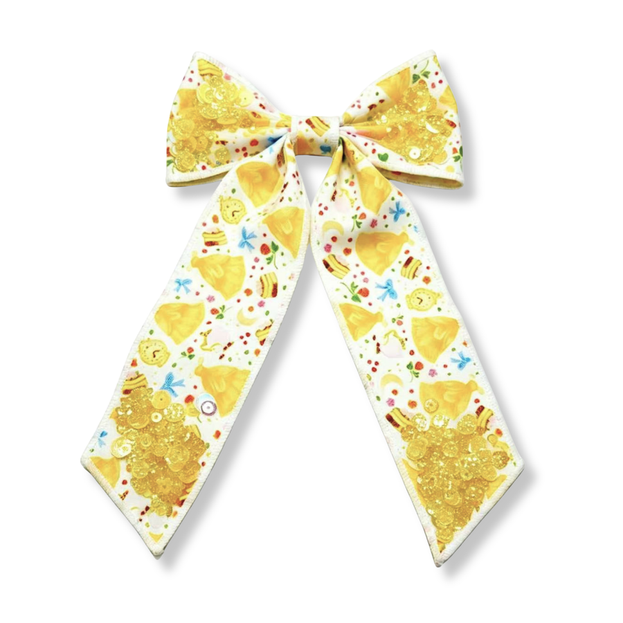 This elegant princess-inspired bow features a white background adorned with yellow ball gowns, enchanted clocks, slices of cake, bows, flowers, and other fairytale-themed details. Clusters of shimmering gold sequins accent the upper loops and lower tails, adding sparkle and dimension to the design.
 Bow Sizing 5" x 8.5"