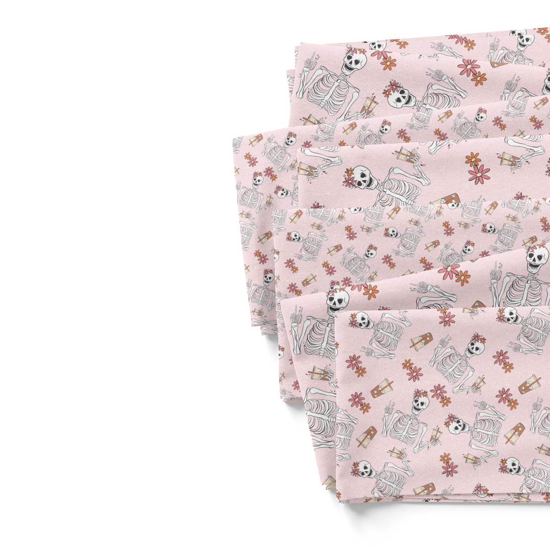 Light pink fabric by the yard fabric swatches with florals and skeletons drinking iced coffee.