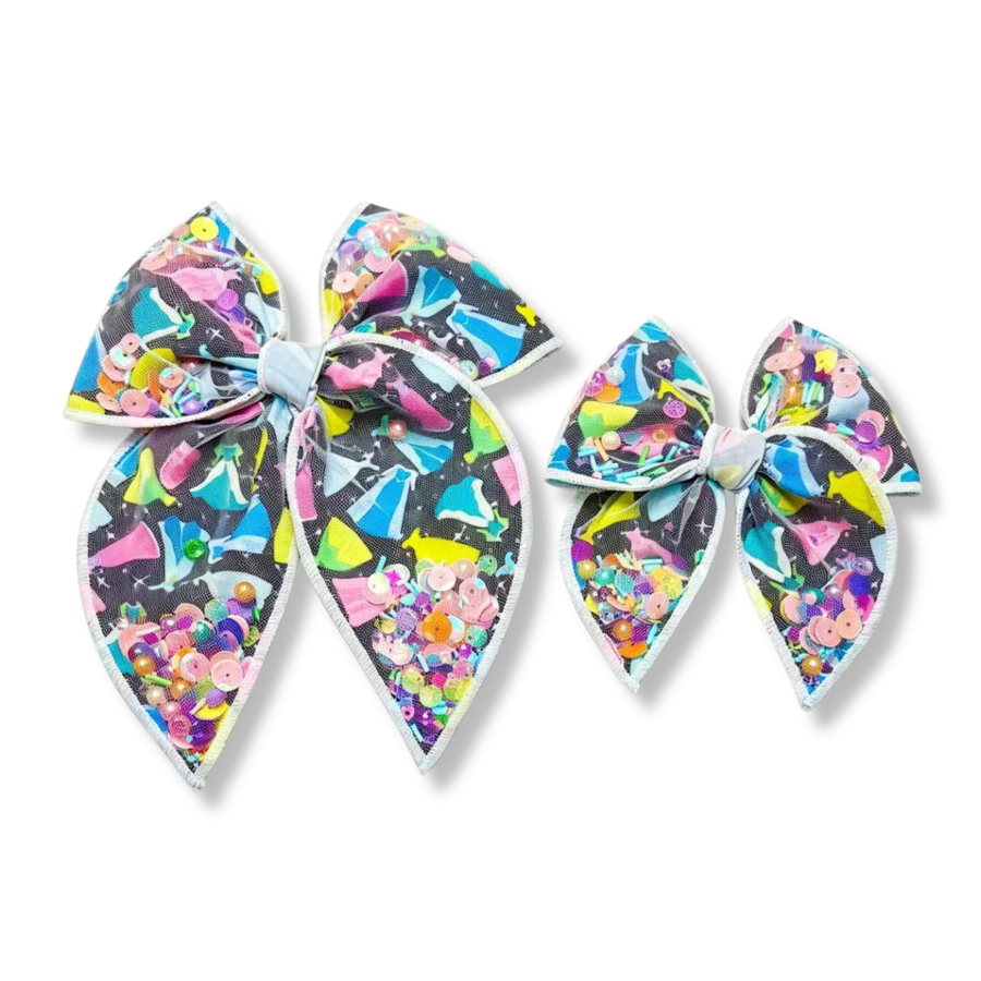 These dazzling shaker bows feature a black background printed with colorful princess-inspired gown silhouettes in shades of pink, blue, yellow, and mint. Filled with pastel sequins, beads, and confetti-like embellishments, the shaker sections create beautiful sparkle, texture, and movement. Available in both a larger statement bow and a smaller matching style, these bows add a magical touch to any outfit.
you pick size
Small 4.5" x 4.5"
Large 6.5" x 6.5"