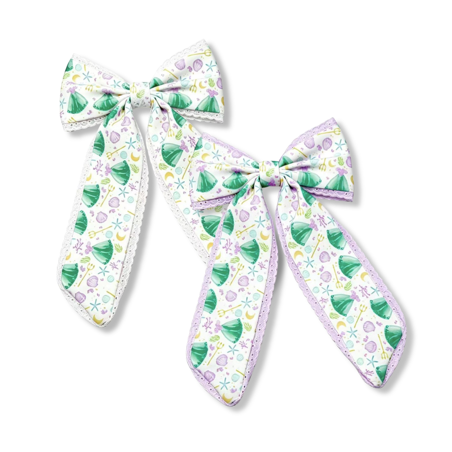 These charming long-tail bows feature a whimsical under-the-sea print with seafoam green mermaid dresses, lavender seashells, starfish, bubbles, and ocean-inspired details on a soft white background. Delicate white or lavender lace trim accents the edges, adding a touch of elegance and texture to the design. The flowing tails and pastel color palette create a magical mermaid-inspired accessory full of seaside charm and storybook beauty. 

you choose white or lavender lace trim
SIZE:
Large 5.5" X 9.5"