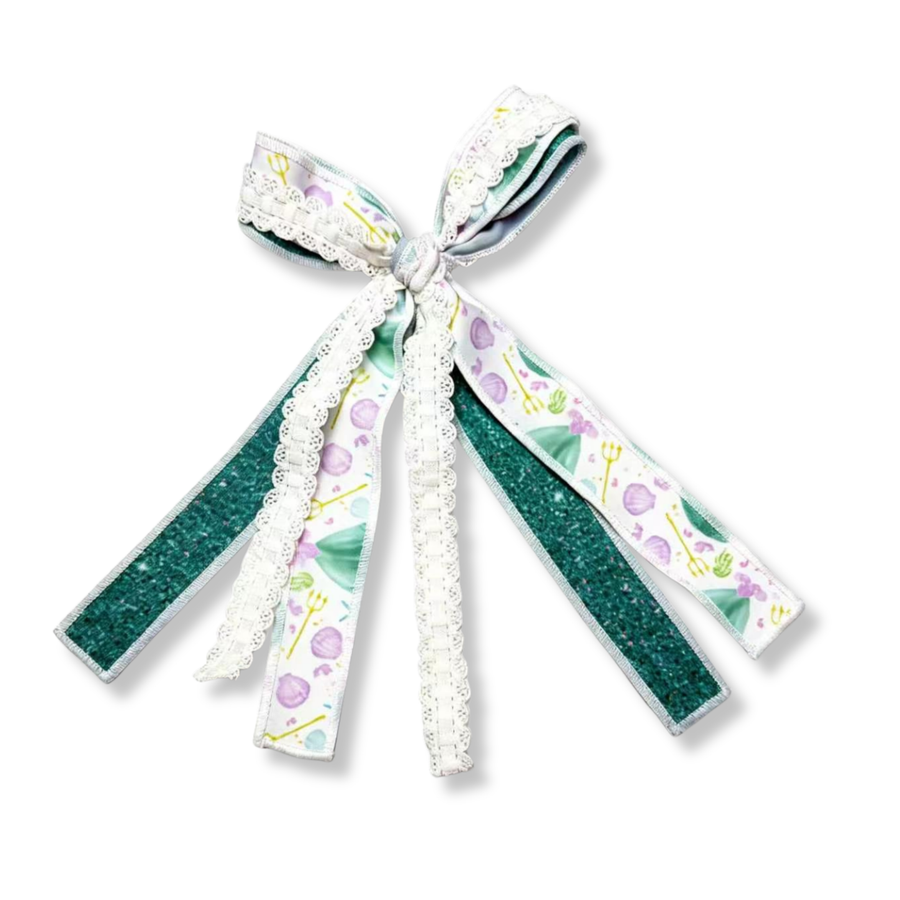 A charming ribbon tie bow crafted from three coordinating ribbons. The design features a whimsical seashell-inspired ribbon in soft lavender and light green dress, a sparkling emerald green glitter ribbon that adds shimmer and contrast, and a delicate white lace ribbon that brings elegant texture and vintage-inspired charm. 

Bow Sizing 4" x 8"