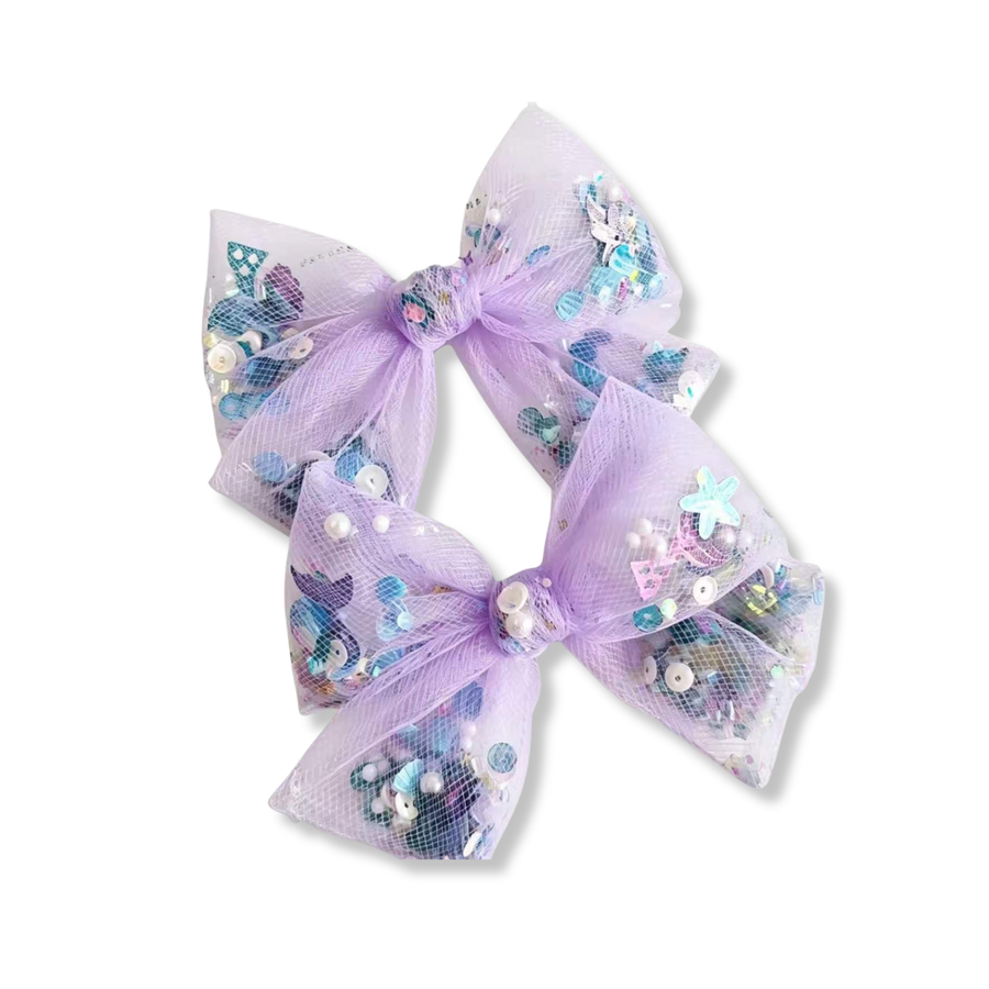
These whimsical bows are crafted from soft lavender mesh and filled with a colorful mix of iridescent sequins, pearls, stars, and ocean-inspired embellishments. The sheer mesh creates beautiful dimension while allowing the sparkling accents to shine through, adding playful movement and shimmer. With their dreamy lavender color and magical under-the-sea details, these bows are full of charm, sparkle, and whimsical elegance. 
MEASUREMENTS

3" x 4"

Set of 2