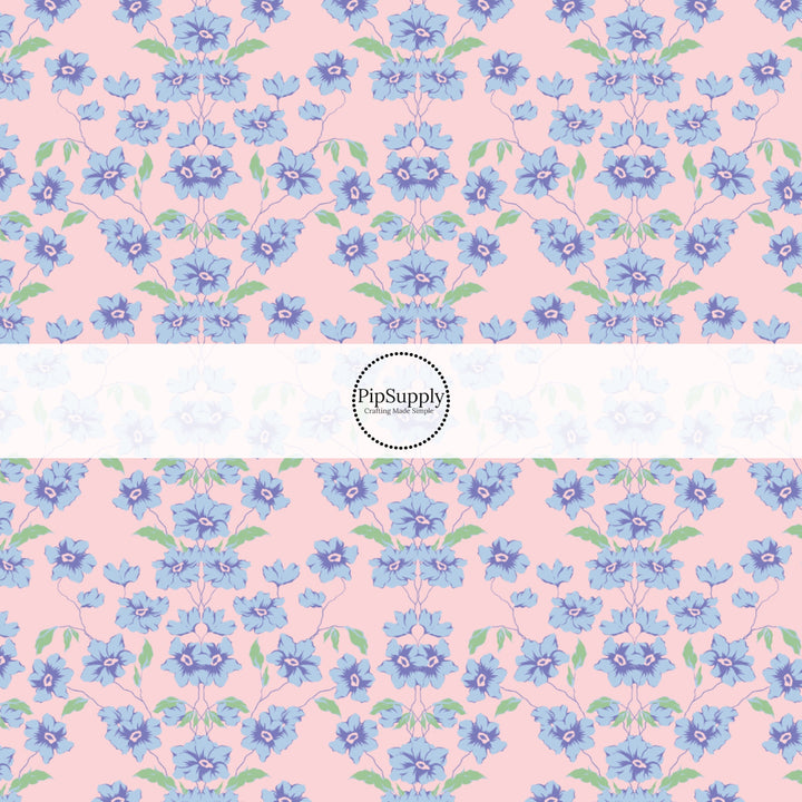 This spring floral themed fabric by the yard features blue flowers on pink. This fun pattern fabric can be used for all your sewing and crafting needs!