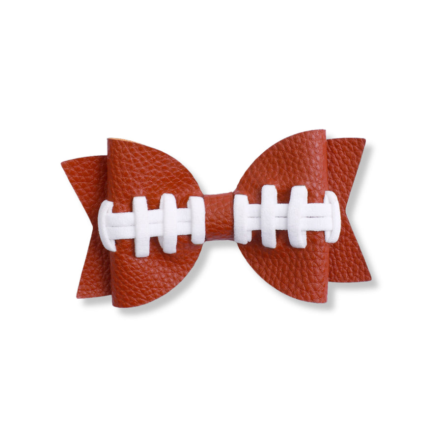 A layered faux leather hair bow in a textured reddish-brown finish, styled to resemble an American football. The bow features rounded loops, pointed tails, and white football lace detailing across the center, secured with a matching center wrap. The sporty design combines classic bow styling with football-inspired elements for a fun game-day look.
Approx 3.75"x4.5"