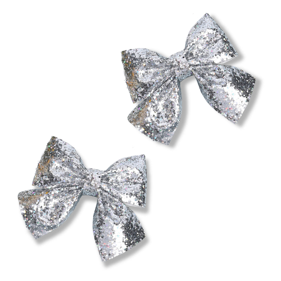 A classic boutique-style hair bow crafted from silver chunky glitter material with an all-over sparkling finish. The bow features full, structured loops, softly tapered tails, and a matching center wrap. The reflective glitter catches the light from every angle, creating a bright, shimmering effect that adds a touch of glamour and sparkle to any hairstyle.
