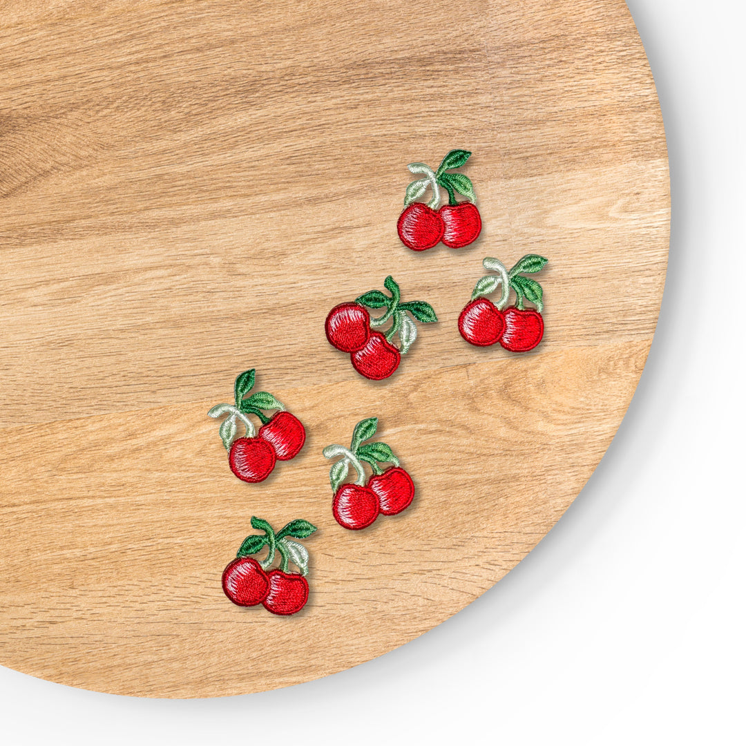 This embroidered cherry iron-on applique features two bright red cherries with a glossy stitched finish, connected by delicate stems and accented with vibrant green leaves. *APPROX .75" Tall X 1" 
