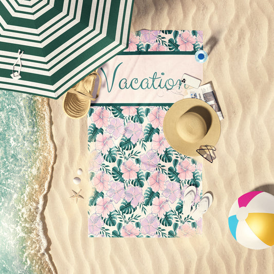 Hibiscus and palm leaves print beach towel laid out by the shore.