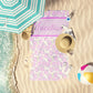 Lavender mermaid seashell print beach towel laid out by the shore.