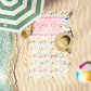 Pastel Multi Seals print beach towel laid out by the water at the beach.