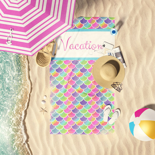 Rainbow ombre scales print beach towel laid out by the water at the beach.