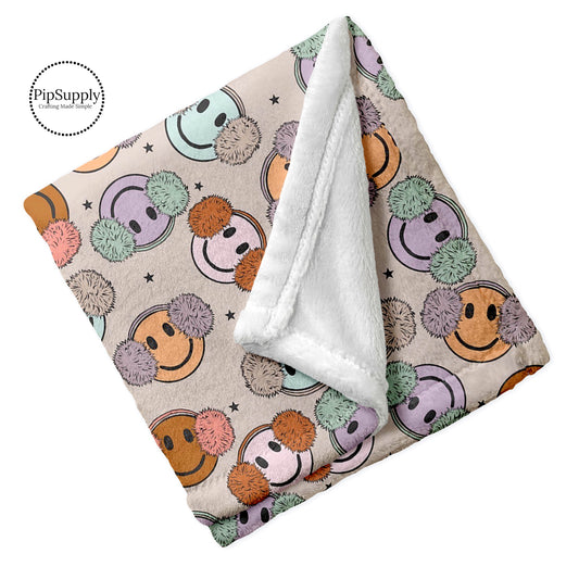 Folded minky blanket with pastel colored smiley faces with fuzzy earmuff pattern.