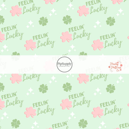 Words written in green that say "feelin' lucky" with pink and green clovers and white sparkles on a green bow strip