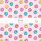 pink, yellow, and blue smiley face print on light pink fabric by the yard
