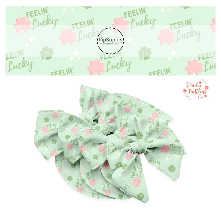 Green tiny clovers with pink clovers and words that say "feelin' lucky" on a pastel green bow strip