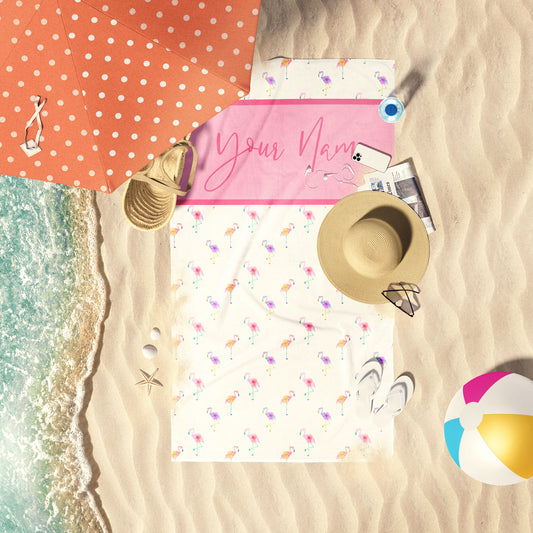 Watercolor flamingos print beach customizable towel laid out on the shore.