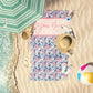 Butterfly bloom print beach personalized towel laid out by the water on the sand.