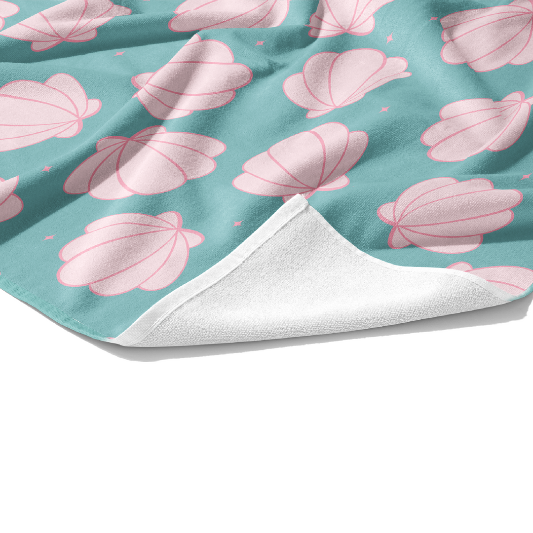 Plush white cotton towel with light pink seashells on aqua pattern print on the front.