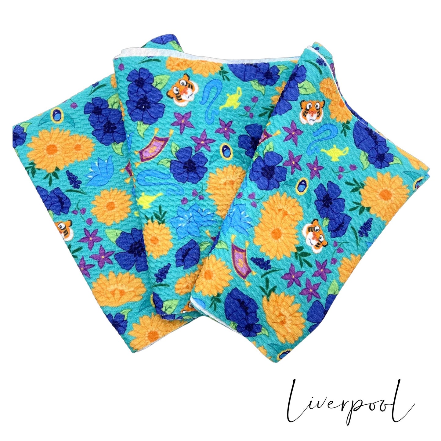 Folded aqua Liverpool stretch fabric strip with royal, golden yellow, and purple floral princess pattern including flying carpets, tiger face, and magic lamps.