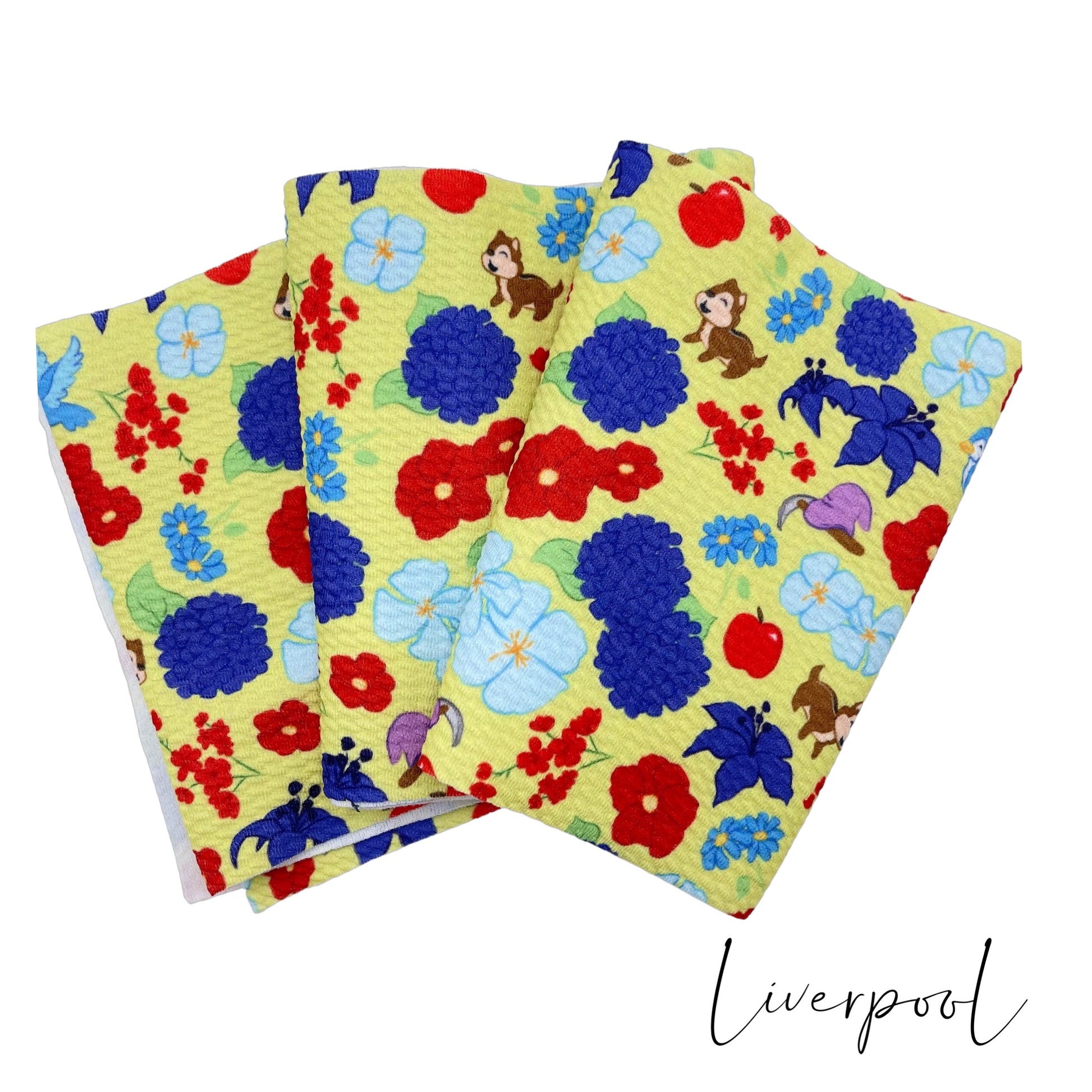 Folded yellow Liverpool stretch fabric strip with royal, red, and light blue floral princess pattern including chipmunks, hat and axe, apple, and blue bird.