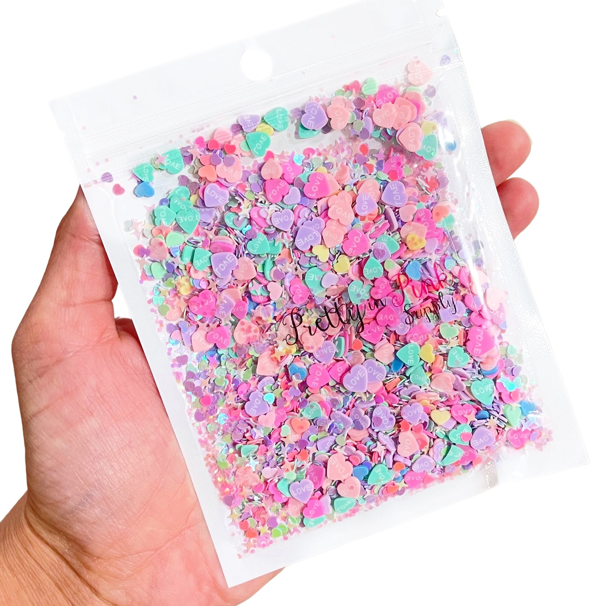 Hand holding bag of pastel heart polymer clay slice mix and sequin mix.