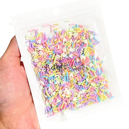 Hand holding bag of pastel sprinkles and white heart clay slices.