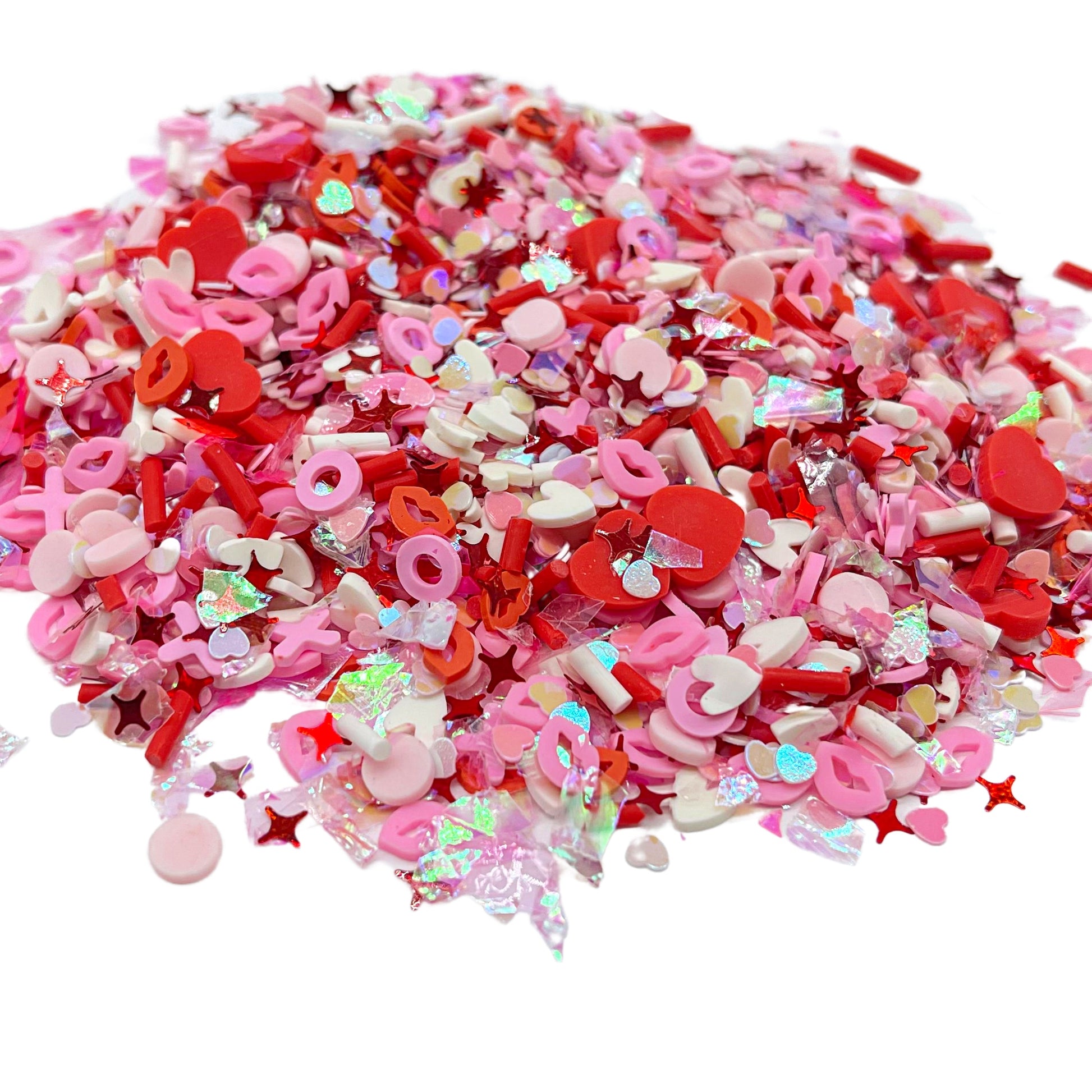 Valentine polymer clay slices mix with red hearts, pink xs and os, white hearts, red sprinkles, and sequin hearts and sparkles poured out of bag.