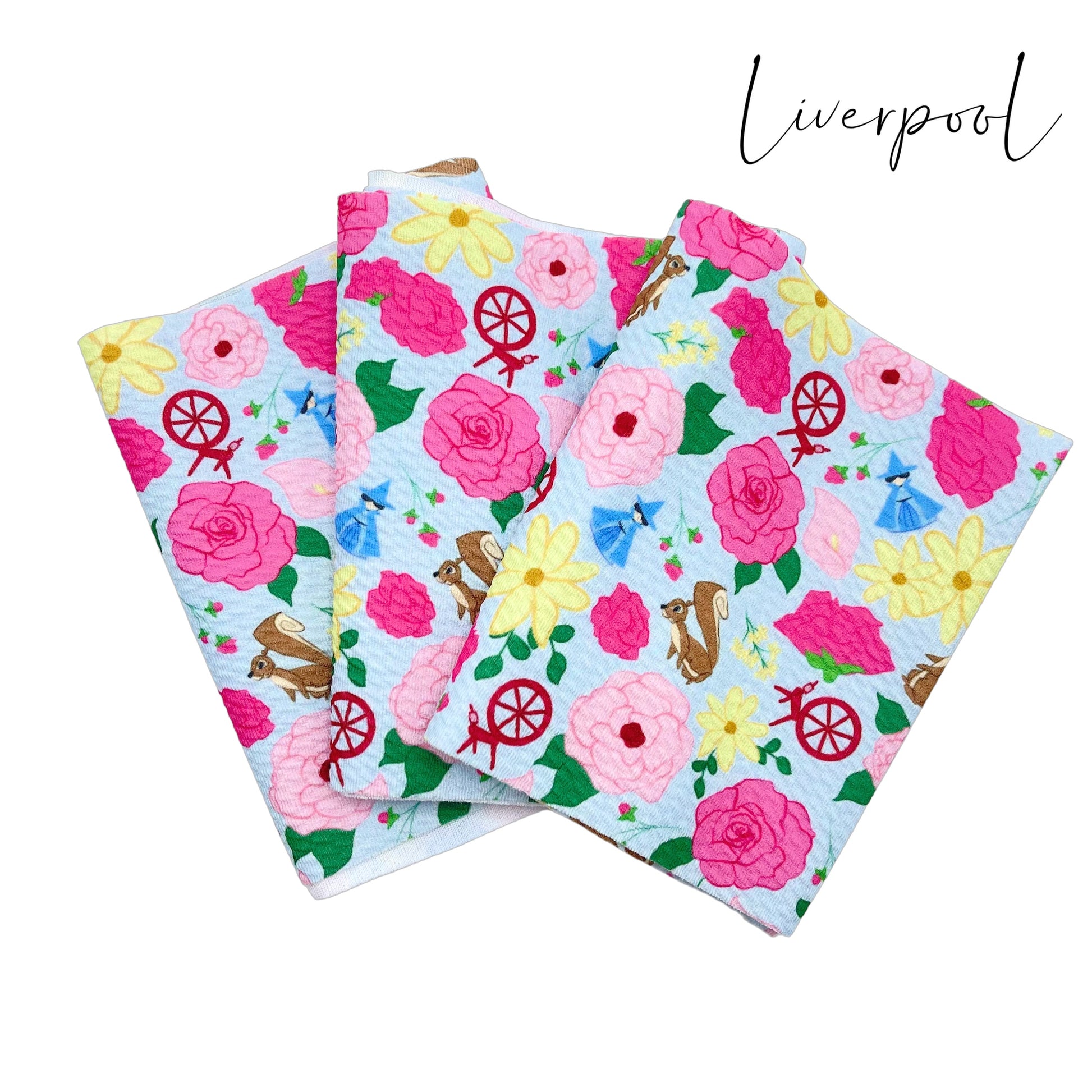 Folded light blue liverpool fabric with hot pink, light pink, and yellow floral princess pattern including squirrels, blue fairy, and spinning wheels.