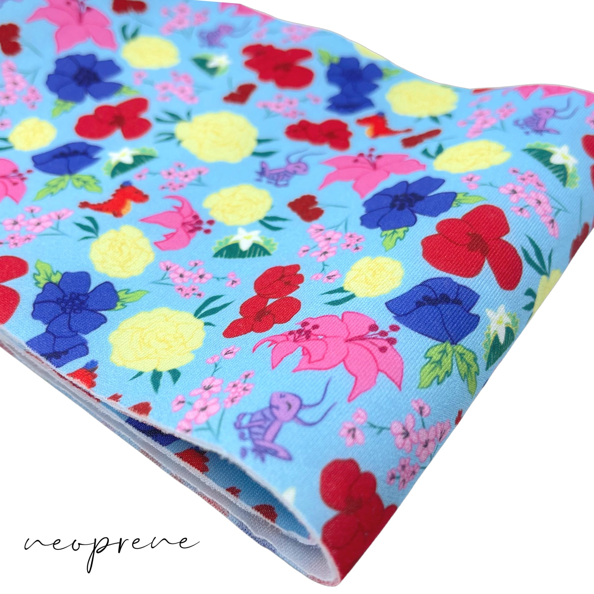 Folded light blue neoprene fabric with yellow, pink, royal blue, and red floral princess pattern including crickets, hair clips, and a red dragon.